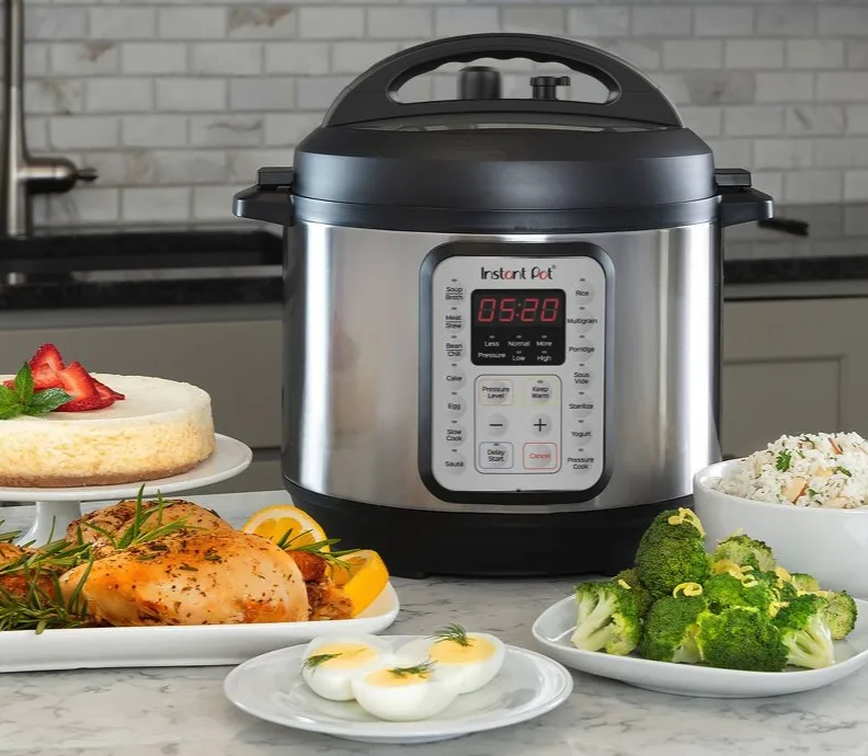 An Instant Pot pressure cooker on a marble countertop surrounded by plates of food including broccoli, rice, eggs, cake and more.