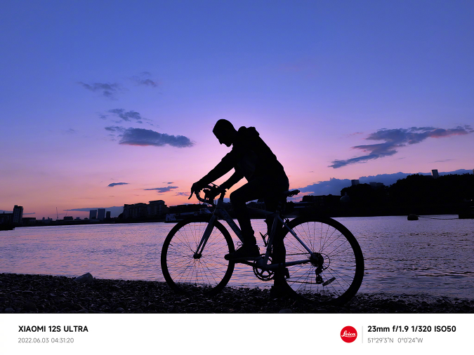 使用小米 12S Ultra 拍摄的样张，日出前的清晨，一名骑自行车的人在河岸上。