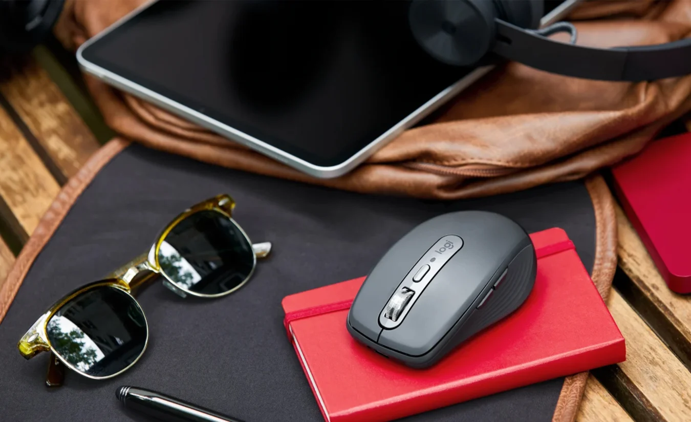 The Logitech MX Anywhere 3 sits atop a notebook next to sunglasses and a tablet.