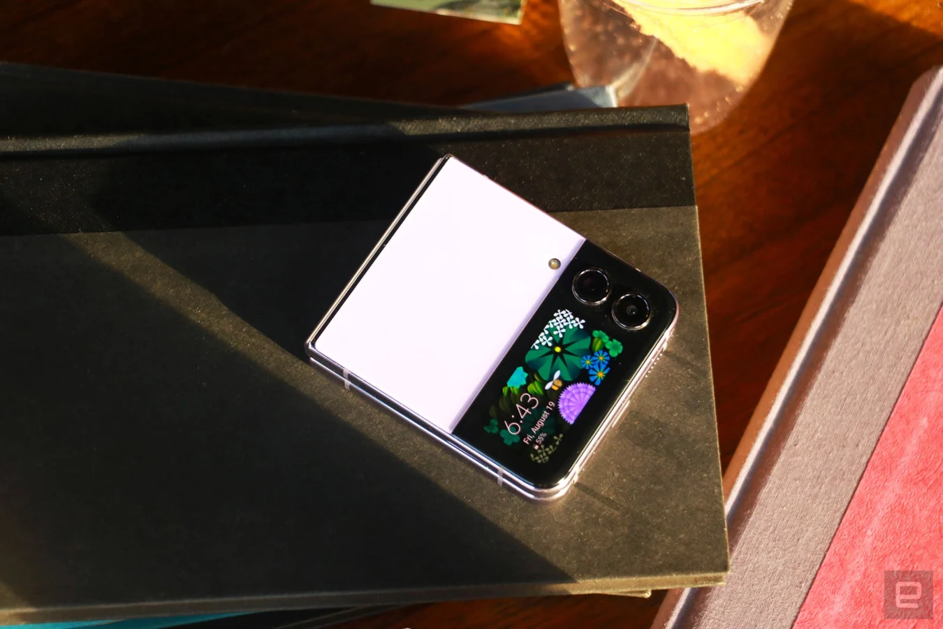 Das Galaxy Z Flip 4 lag geschlossen, mit dem Cover-Display nach oben, auf einem leicht überladenen Schreibtisch.