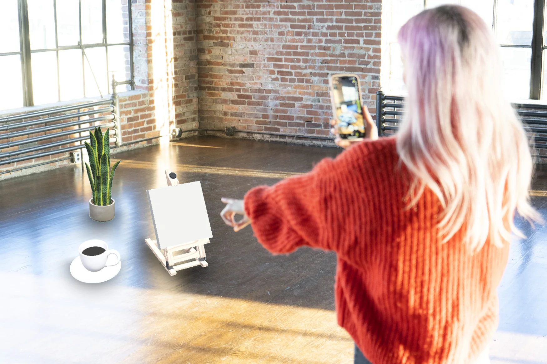 A woman wearing a red sweater in an apartment with brick walls points at virtual (AR) objects on the floor in front of her while holding a phone in AR view.