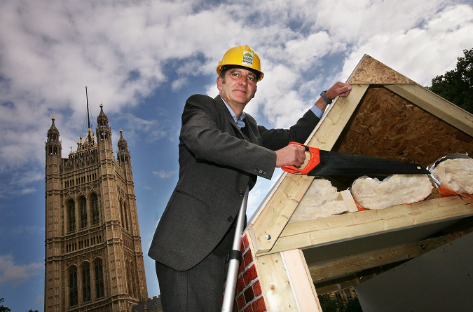 LONDON, ENGLAND - JULY 14: Grand Design's Kevin McCloud holds a saw beside a mock-up insulated loft during a Green Home Refurbishment Programme photocall, outside Parliament on July 14, 2009 in London, England. The TV presenter is making a case to the government to launch a nationwide green refurbishment programme by encouraging people to insulate their homes properly. (Photo by Dan Kitwood/Getty Images)
