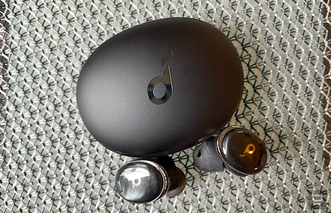 Black wireless earbuds and their charging case on a chain metal background.