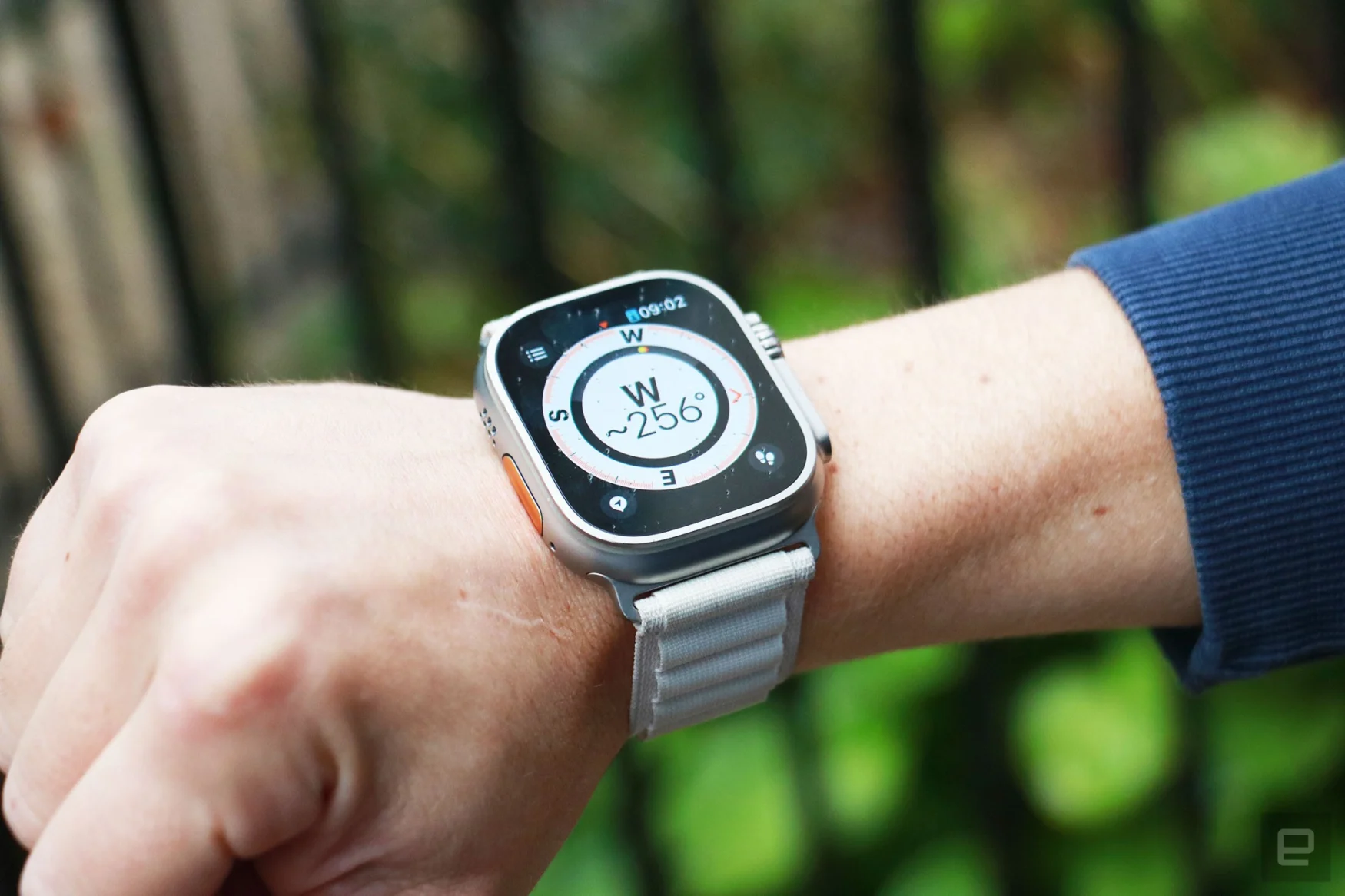 L'Apple Watch Ultra sur un poignet tenu dans les airs avec une boussole sur son écran.  La boussole affiche la lettre W avec 