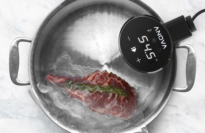 El Anova Precision Cooker Nano sentado en una olla con agua cocinando un trozo de carne.