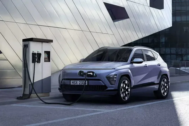 Promotional photo of the new Kona EV parked in front of some futuristic buildings while charging.