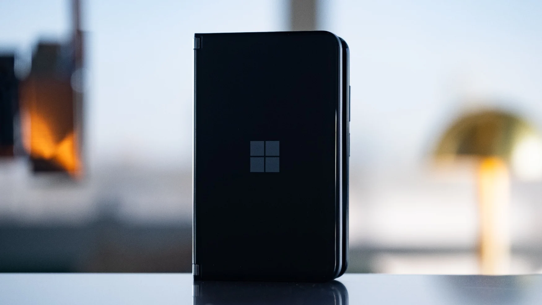 The Microsoft Surface Duo 2 stands almost closed, with the logo on its back facing the camera.