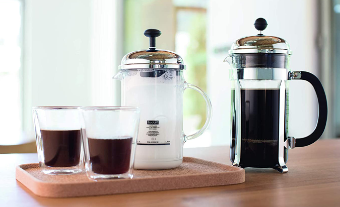 A Bodum Chambord french press on a table with milk and two coffee cups.