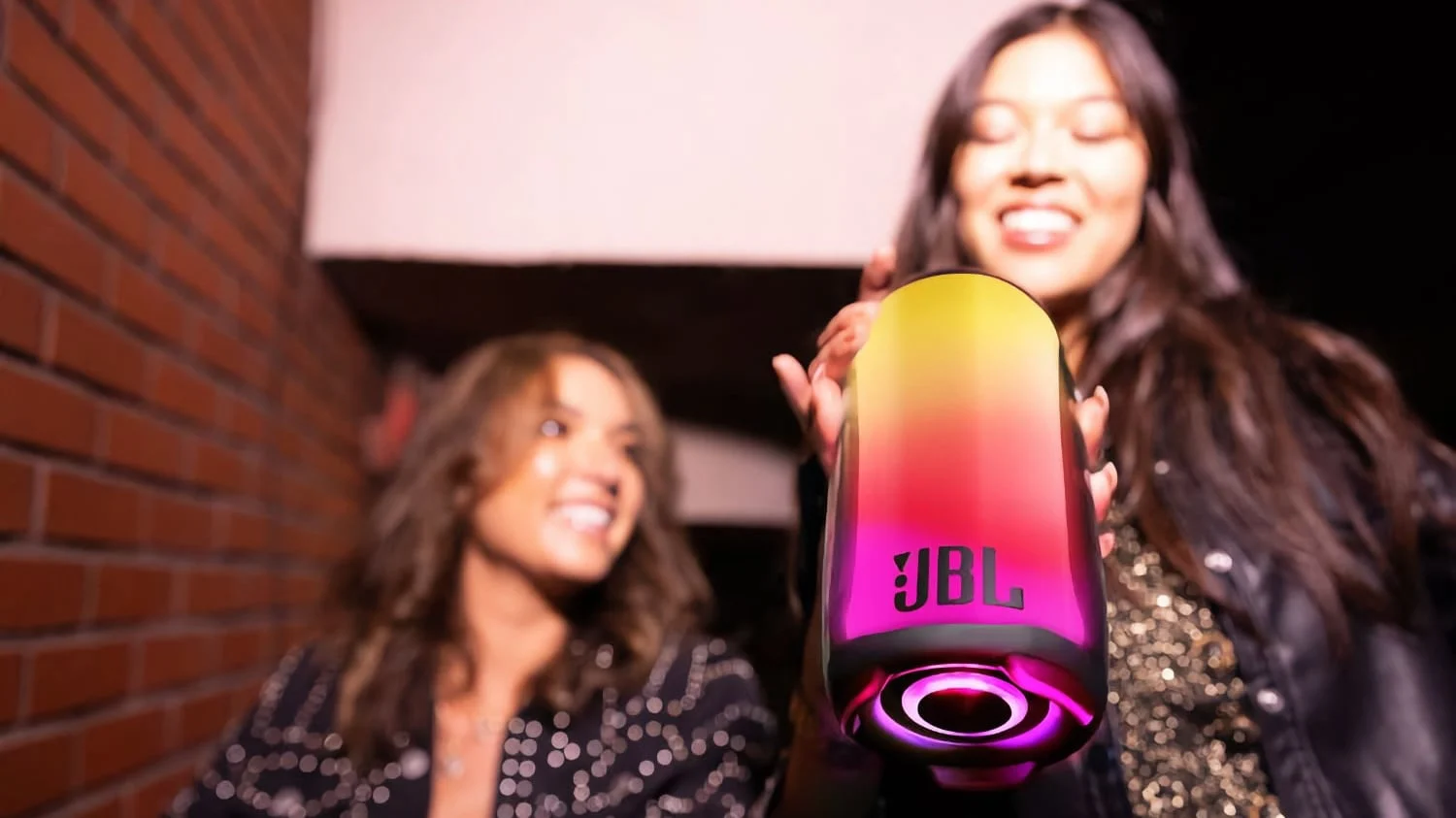 Two women smiling as they listen to the JBL Pulse 5 speaker with its colorful display.