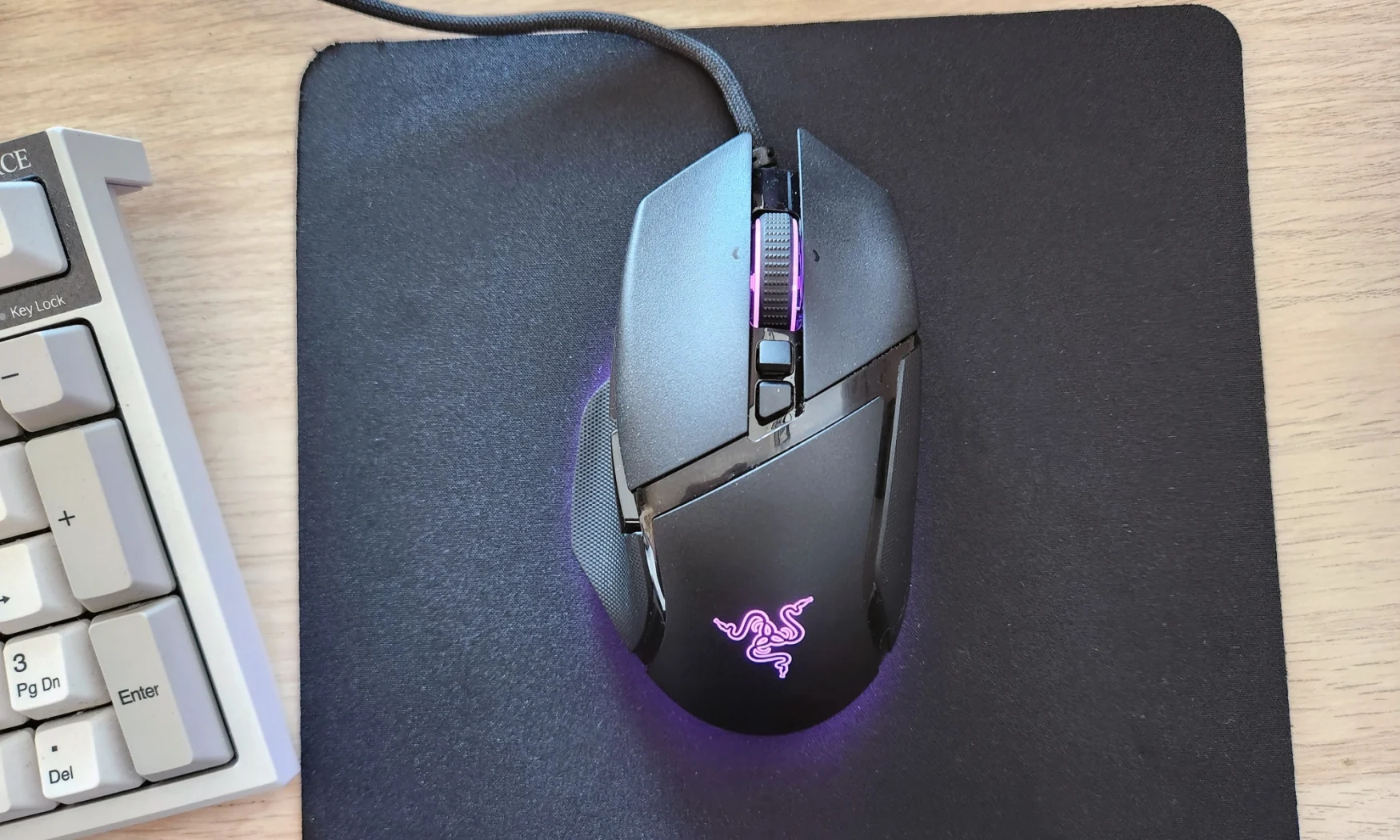The Razer Basilisk V3 gaming mouse rested on a black mouse pad, with RGB lighting emitting from its logo, scroll wheel and underside.