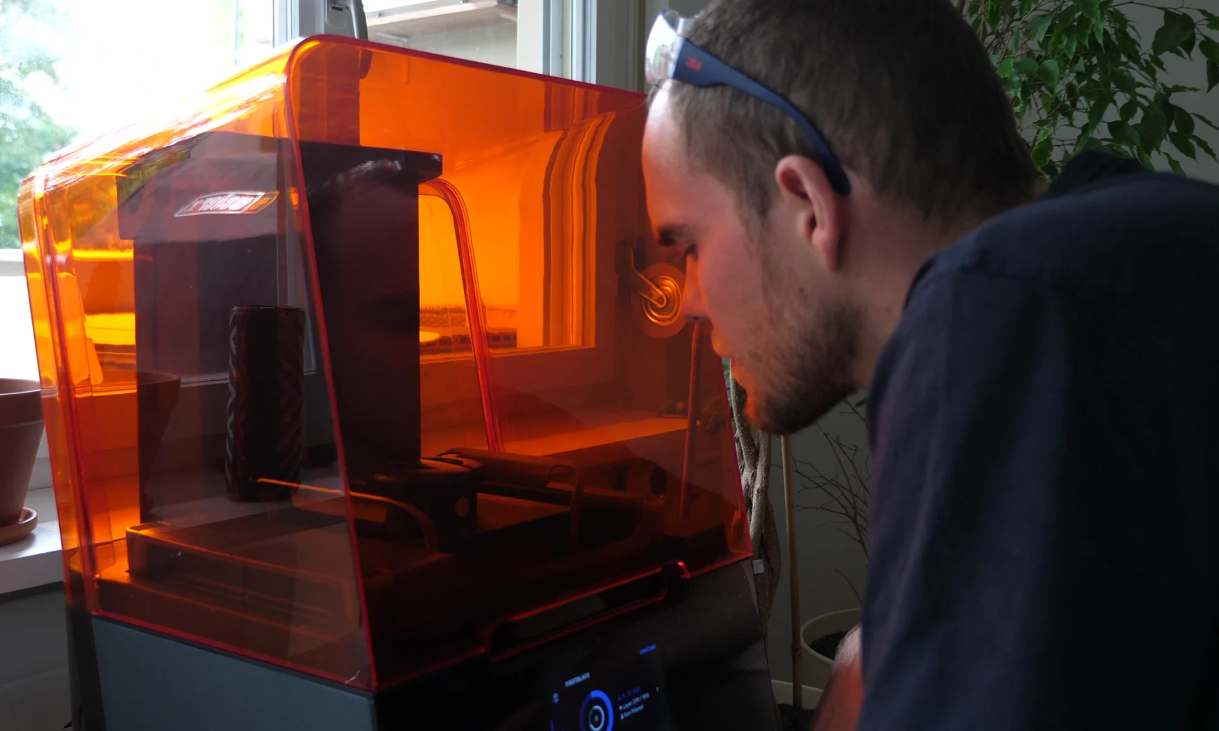 Engineer Ken Pillonel working with a 3D printer. He is to the right / front of the printer, looking inside of it.