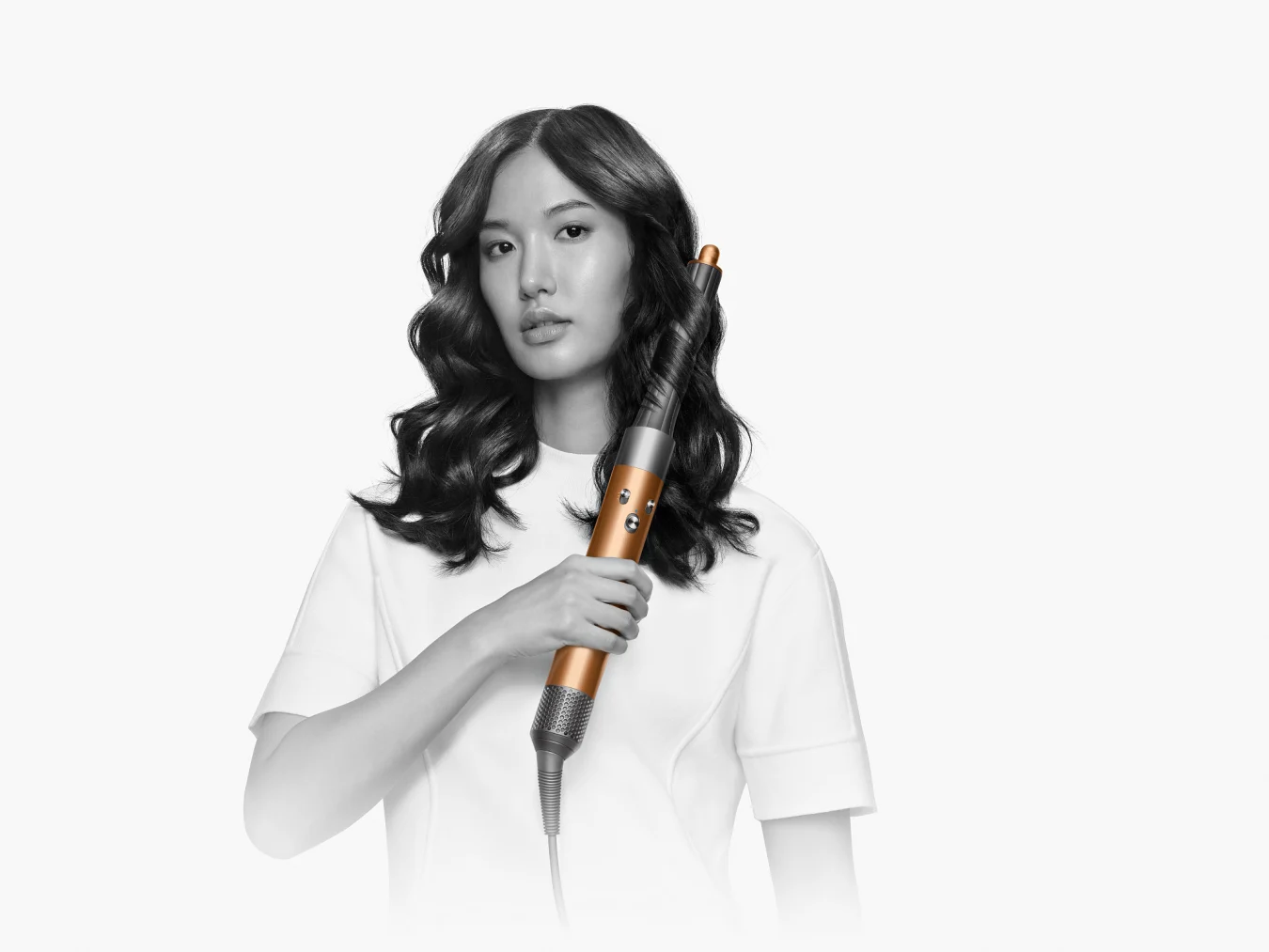 A woman holding the Dyson Airwrap multi-styler 2022 up to her hair, and a strip of her tresses are curled around the rod.