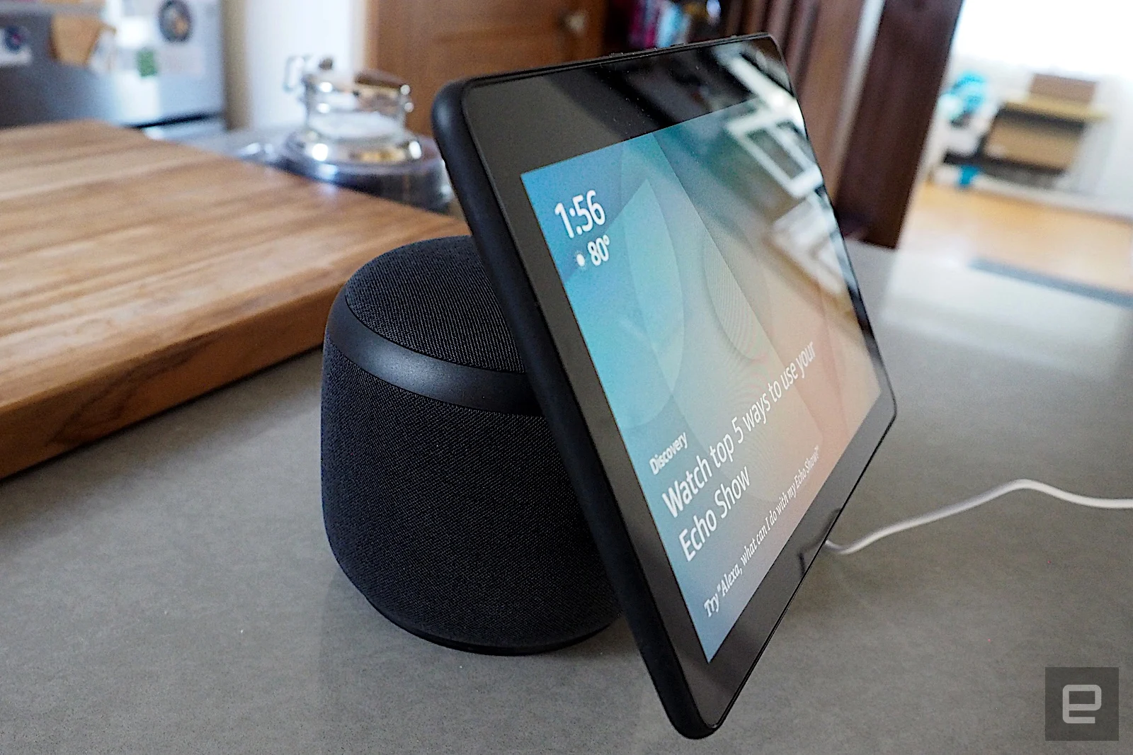 Amazon Echo Show 10 with its screen turned on, sitting on a countertop in front of a wooden cutting board.