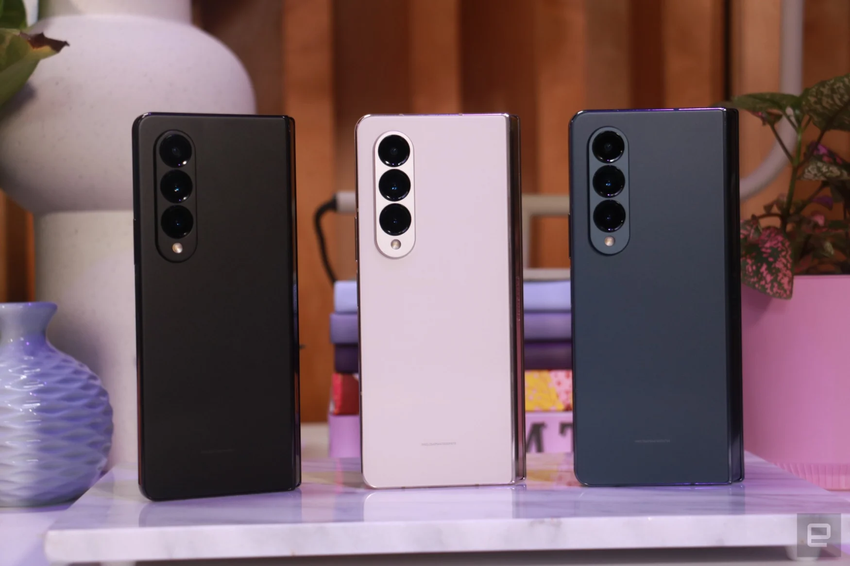 A trio of Galaxy Z Fold 4 standing on a surface, with their triple rear camera systems facing out. 