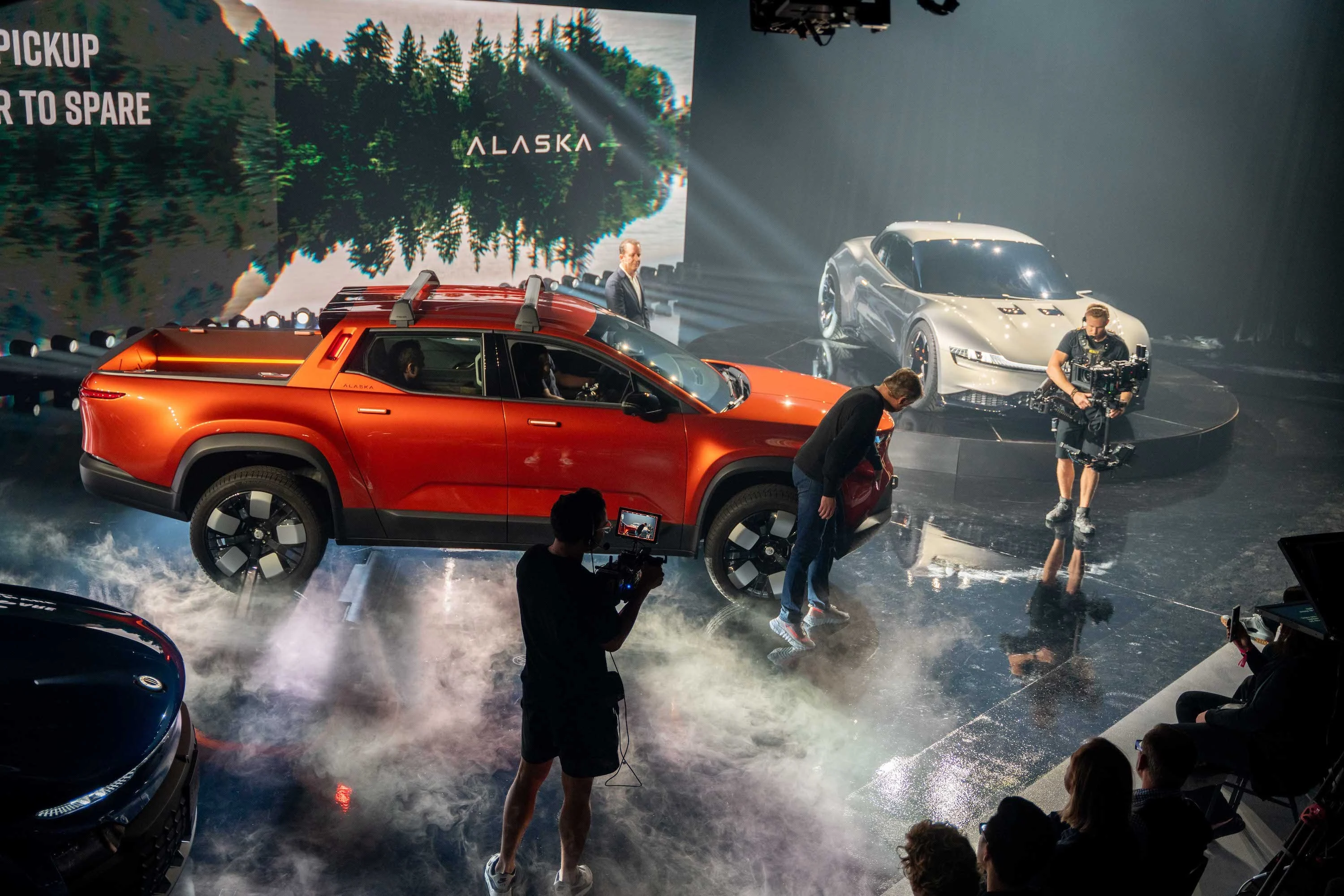 The orange Fisker Alaska electric pickup truck, on stage at an event.