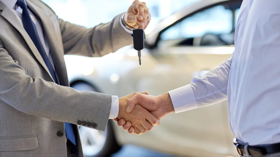 auto business, car sale, deal, gesture and people concept - close up of dealer giving key to new owner and shaking hands in auto show or salon